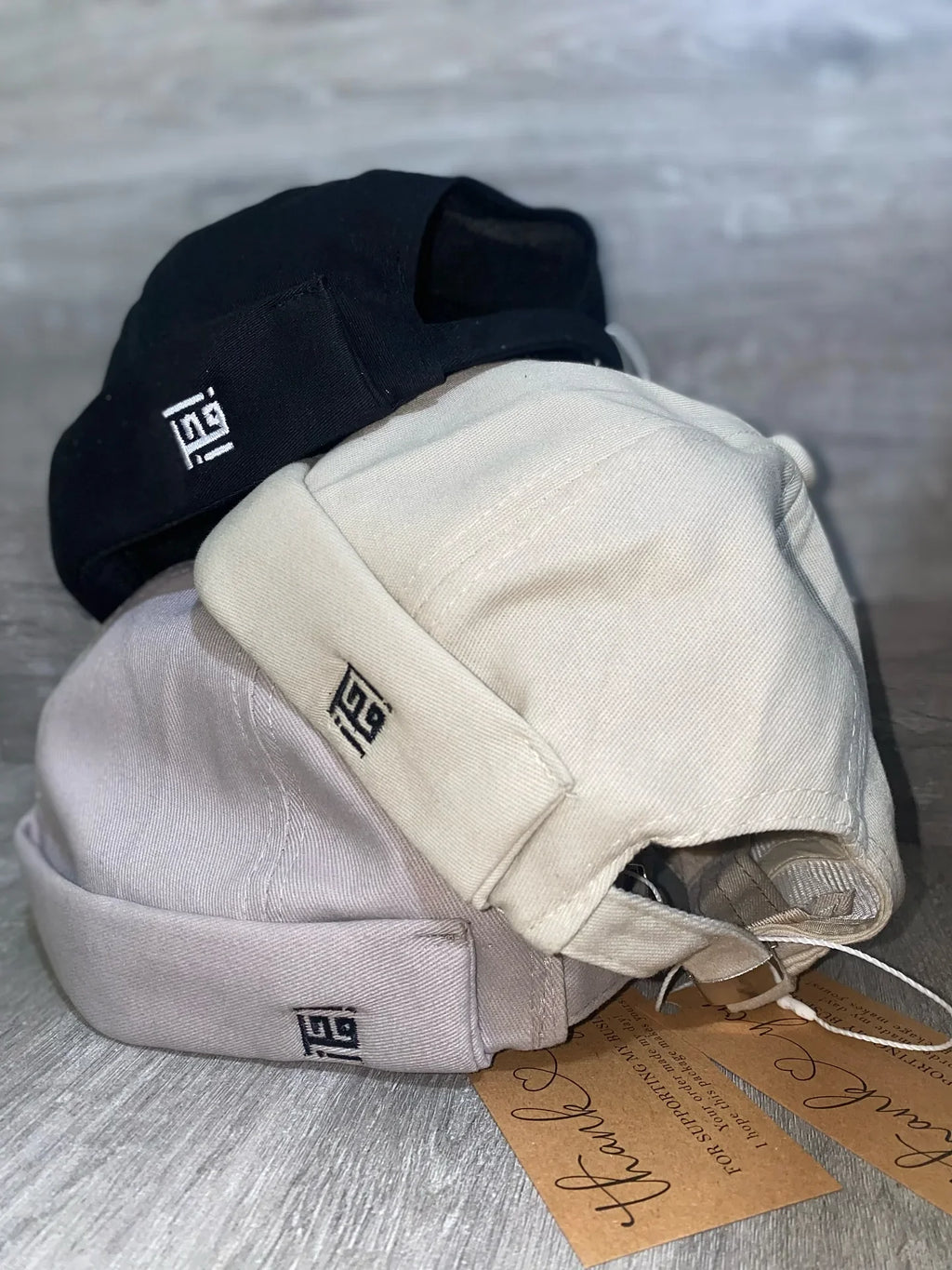 Three caps in black, beige, and gray with a brand logo on a light wooden surface.