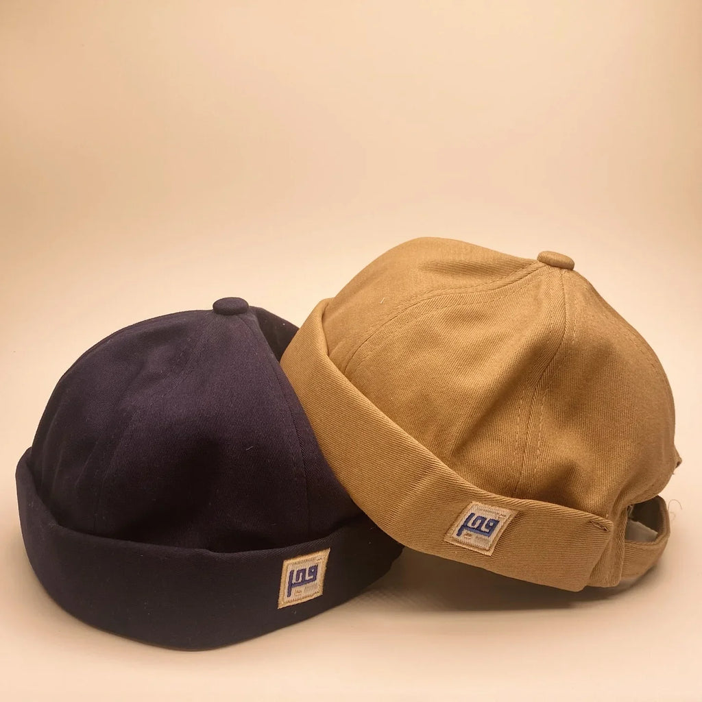 Two caps, one black and one brown, with a visible brand logo on a beige background