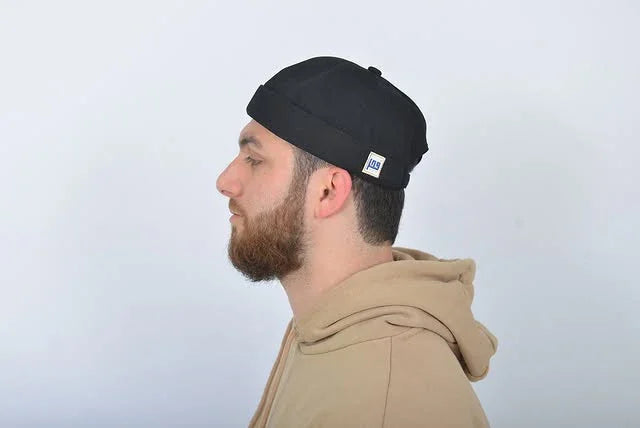 Man wearing a black beanie with a logo on a light gray background