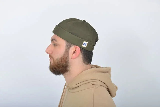 Man wearing a green beanie with a logo on a light gray background