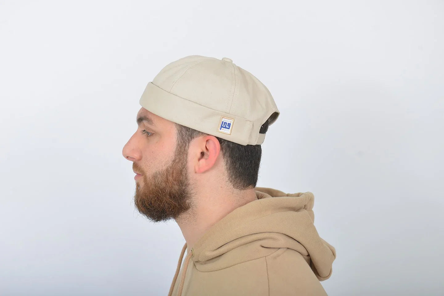 Man wearing a beige cap and hoodie against a white background